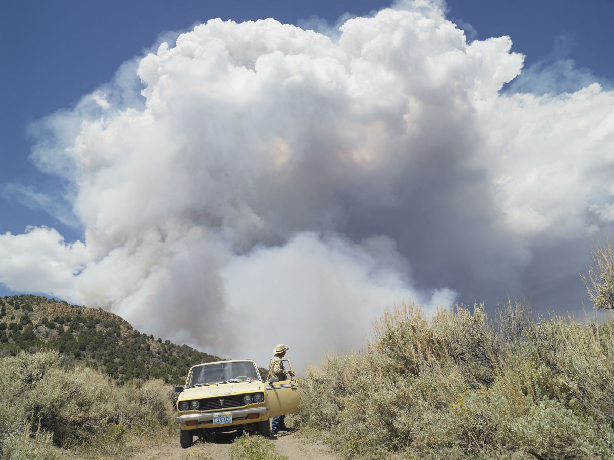  “I met George in Diamond Valley, Nevada. George raised cattle for most of his life. In his retirement, he enjoys chasing forest fires. We drove on dirt roads with dust coming up through the floor of his truck, and then stopped at the hill with the fire burning on the other side. He told me very confidently that he had safety provisions. I asked, “What safety provisions?” And he said: “I have two bottles of water, a Coke, a candy bar, a shovel and a handgun.” In the photograph, which is on the cover of "Frontcountry," the fire cloud arcs over both of us.